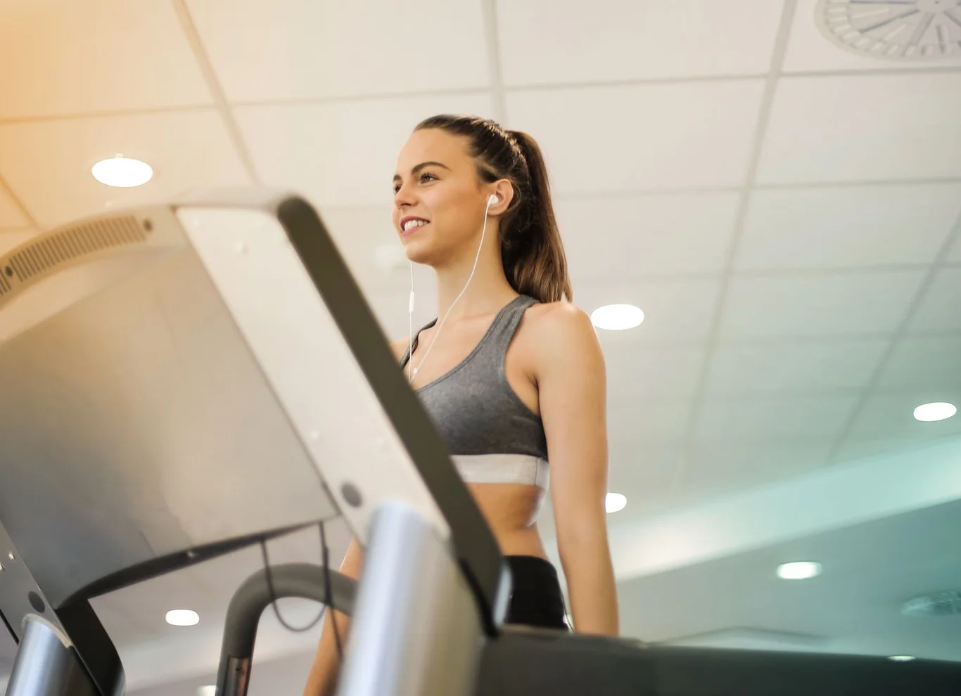 Smiling woman running on a treadmill in a bright gym while wearing earbuds
