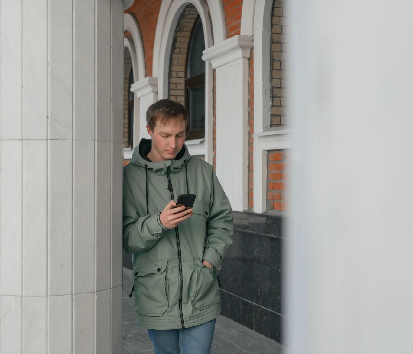 Man in a green hooded jacket checking his phone screen while walking outside