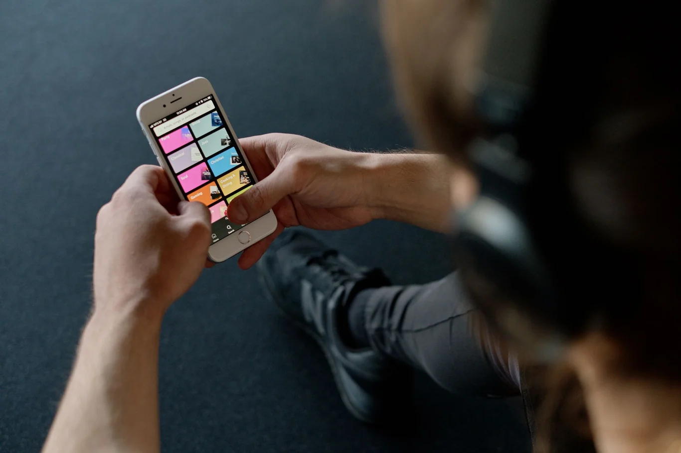 Person wearing headphones sits on the floor checking a colorful phone app
