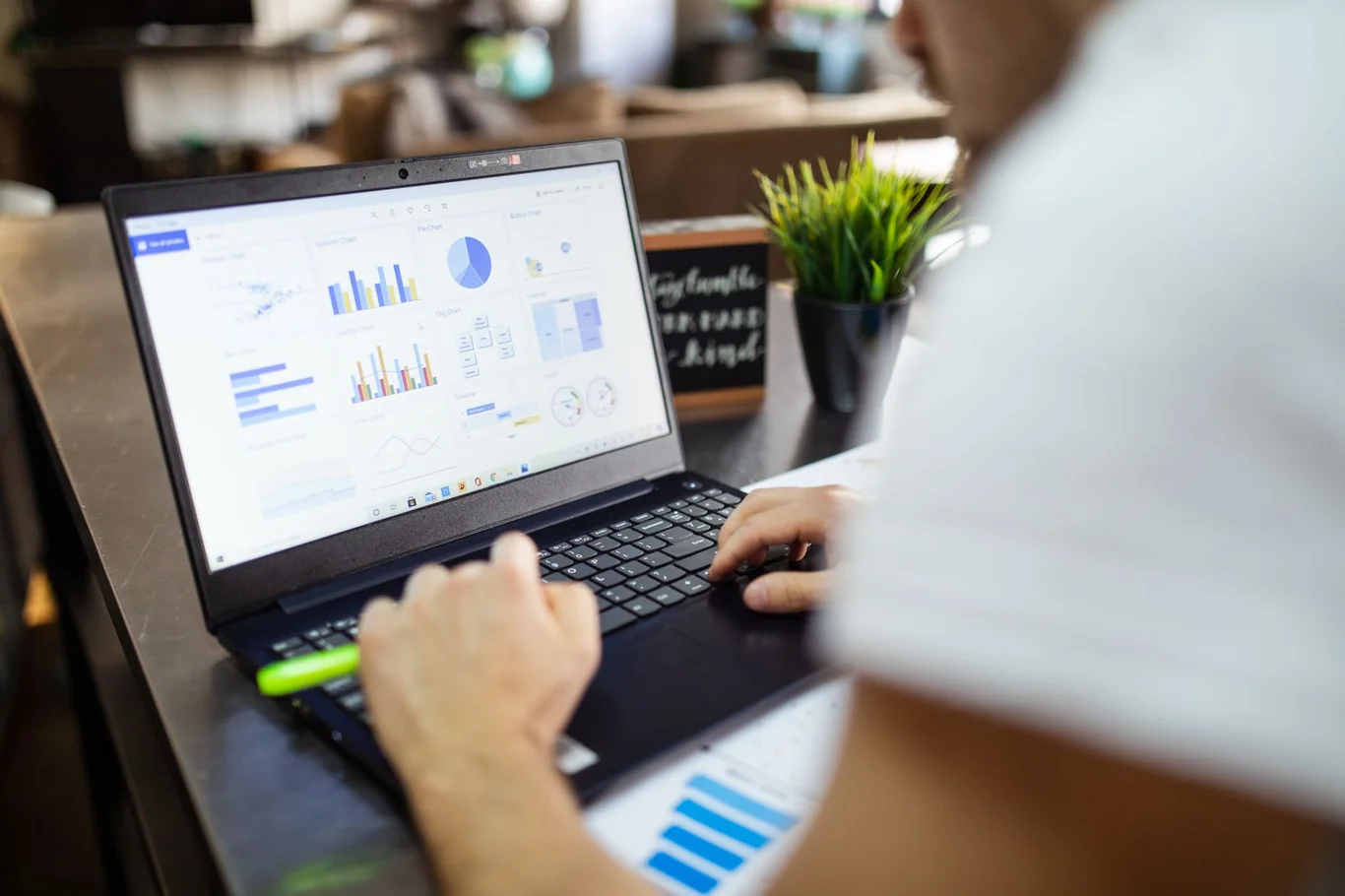 Hands typing on a laptop showing bar and pie charts on a wooden desk