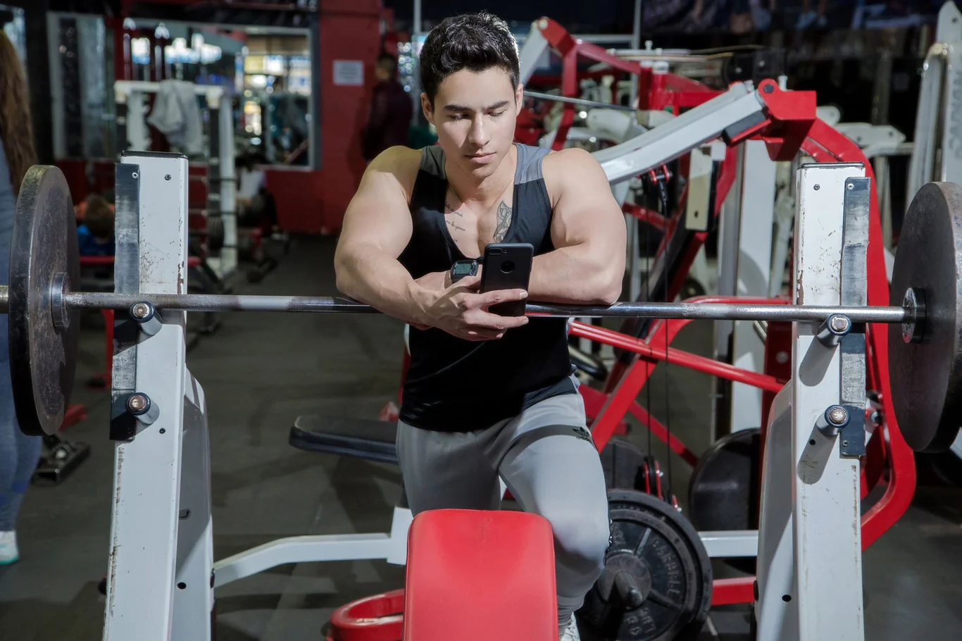 Man sitting at a gym bench checking his phone during a workout