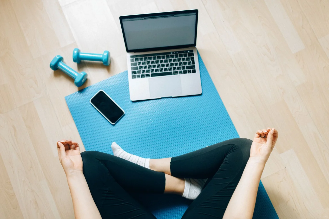 Laptop, phone, and dumbbells arranged on a blue yoga mat for a home workout