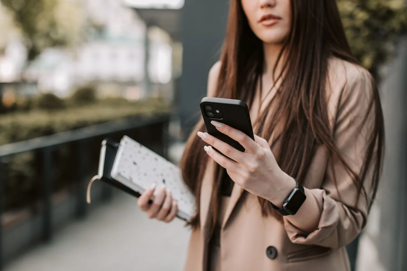 Woman in a beige blazer holding a phone with a smartwatch visible on her wrist