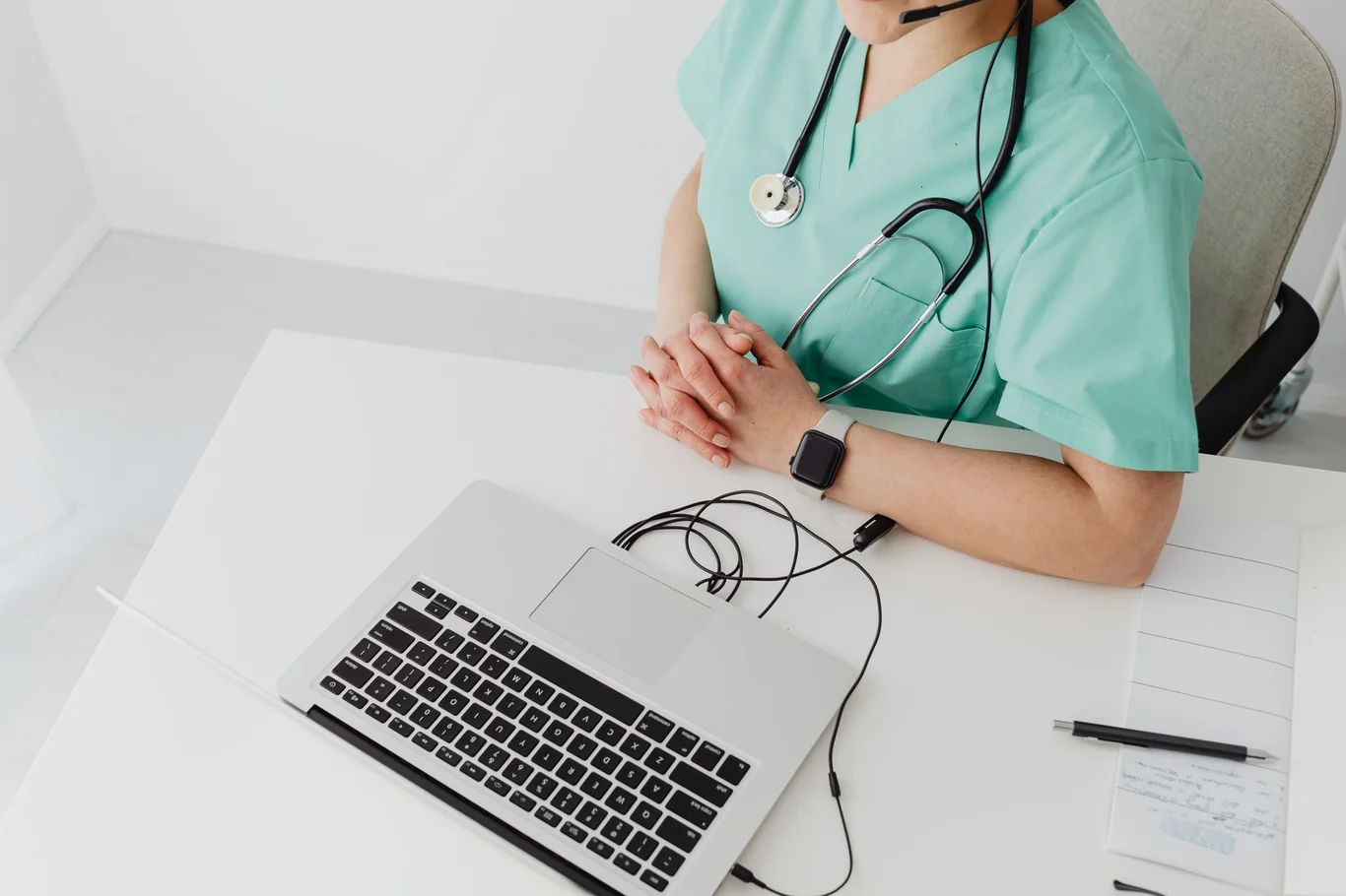 Person in green medical scrubs wearing a smartwatch while typing on a laptop