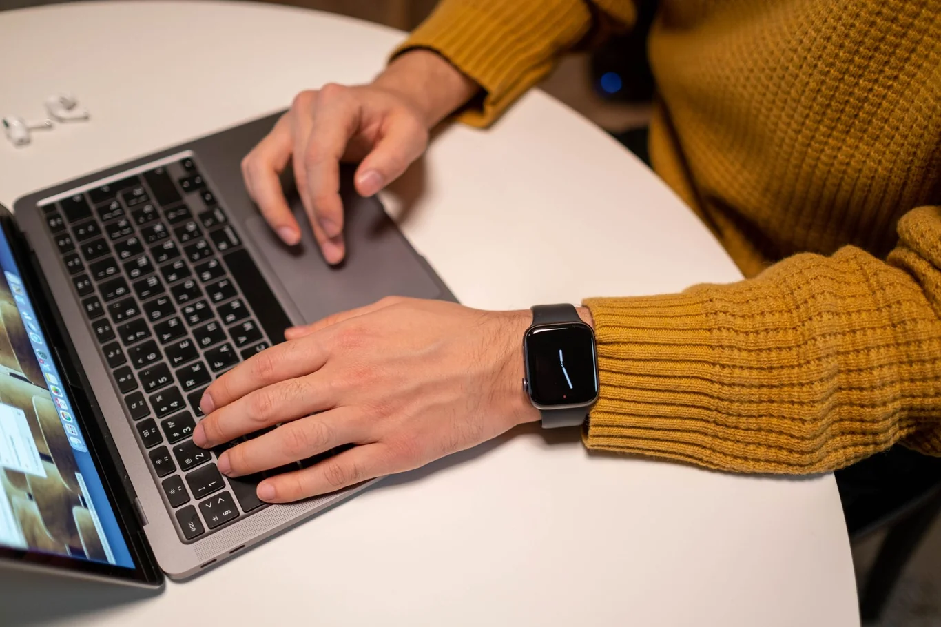 Person in a mustard sweater wearing a smartwatch while typing on a laptop