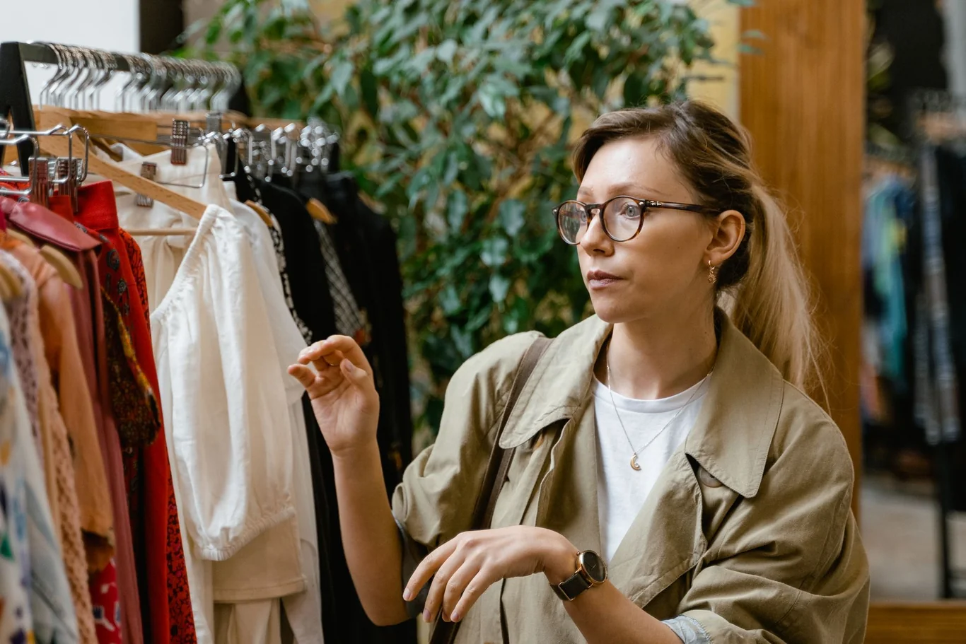 Woman wearing glasses and a wristwatch browsing a clothing rack in a store