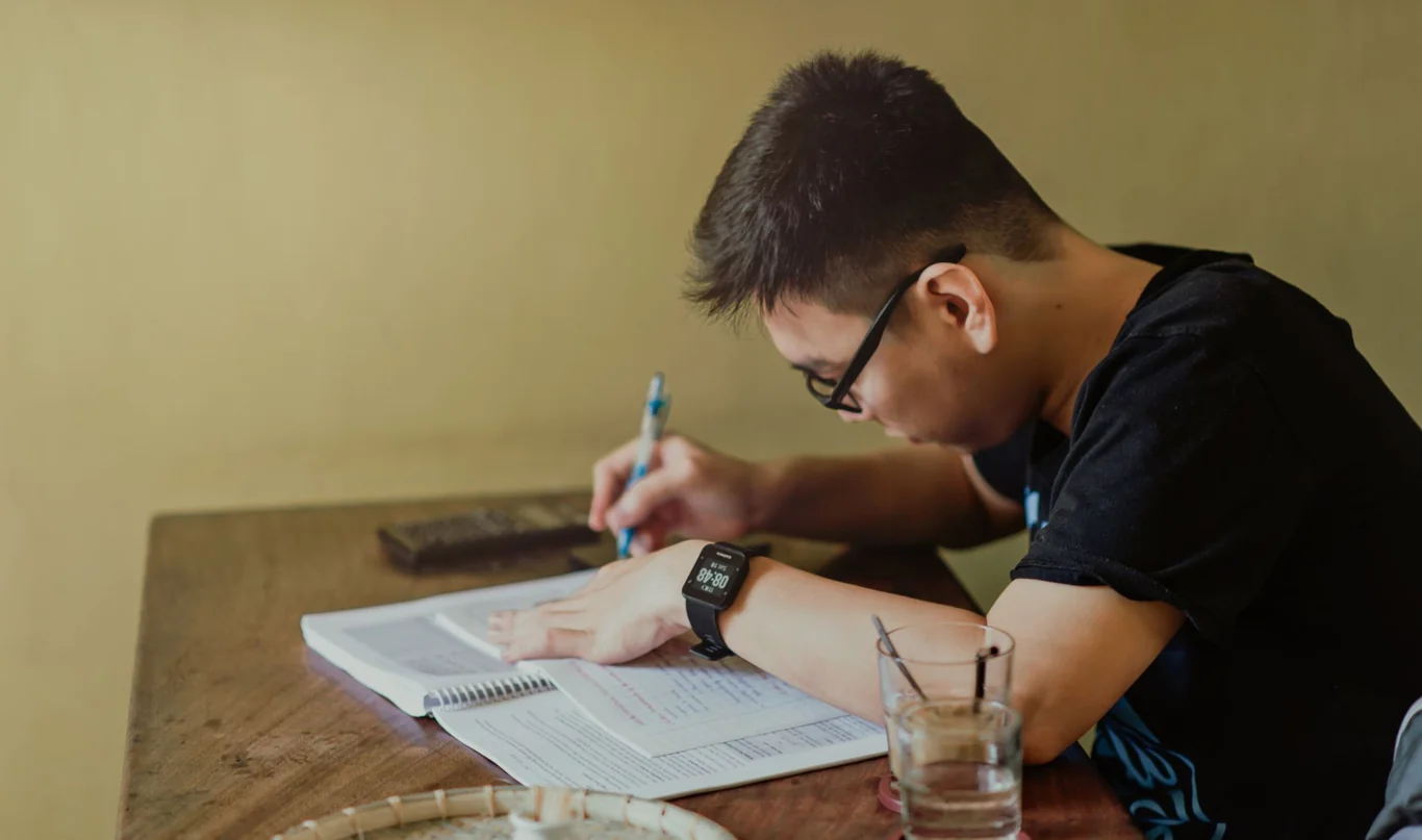 Young man wearing a smartwatch while writing in a notebook at a wooden table