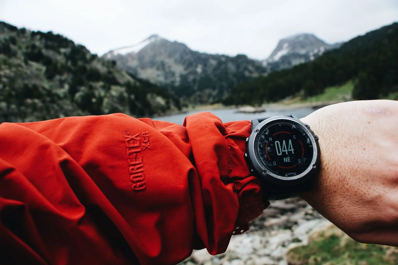 GPS watch on a hiker's wrist showing compass heading with mountains in the background