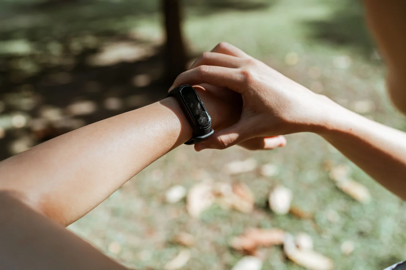 Person checking a black fitness band on their wrist while standing outdoors near fallen leaves