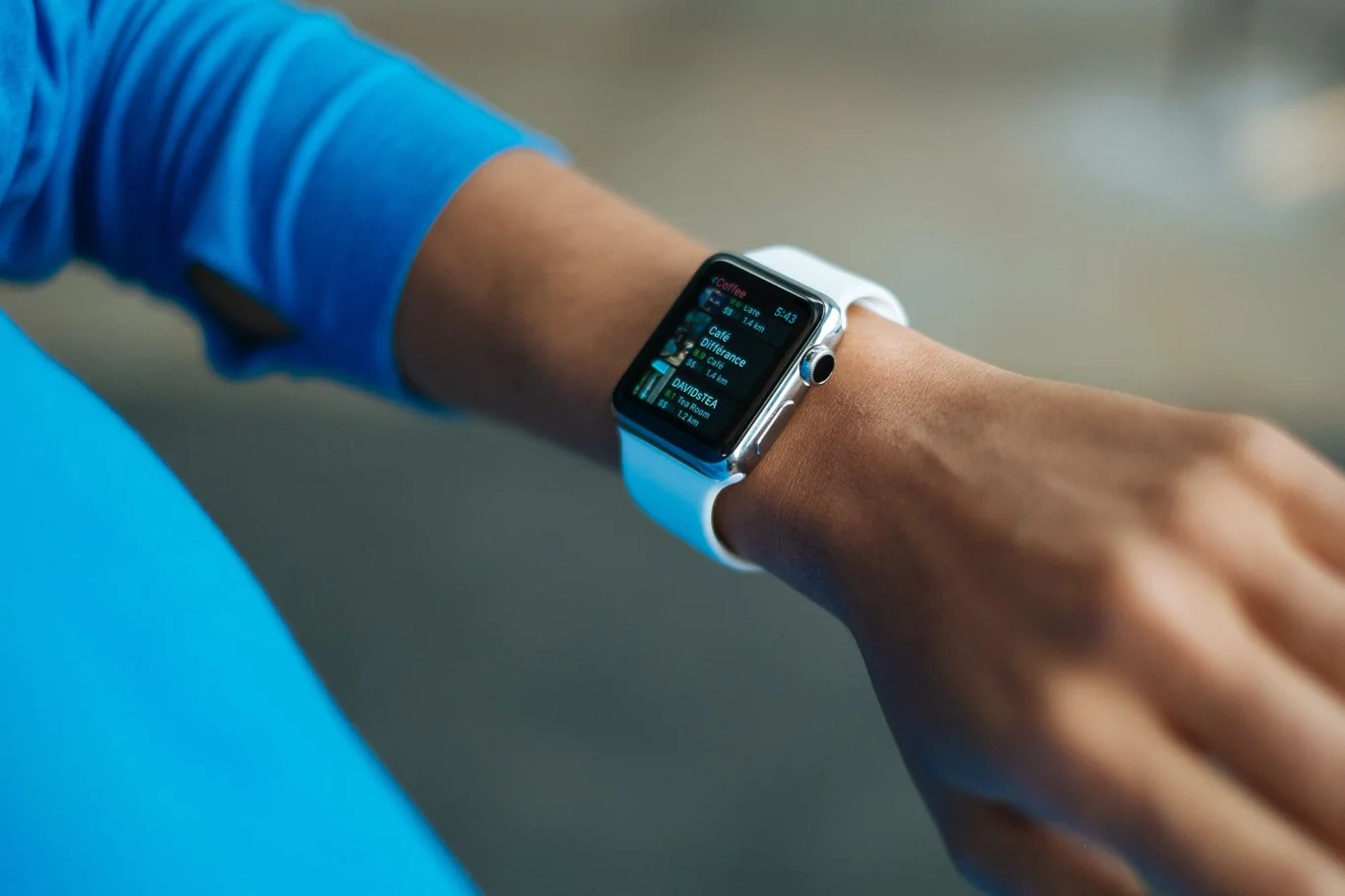 Person wearing a blue long sleeve top checking workout stats on a white smartwatch