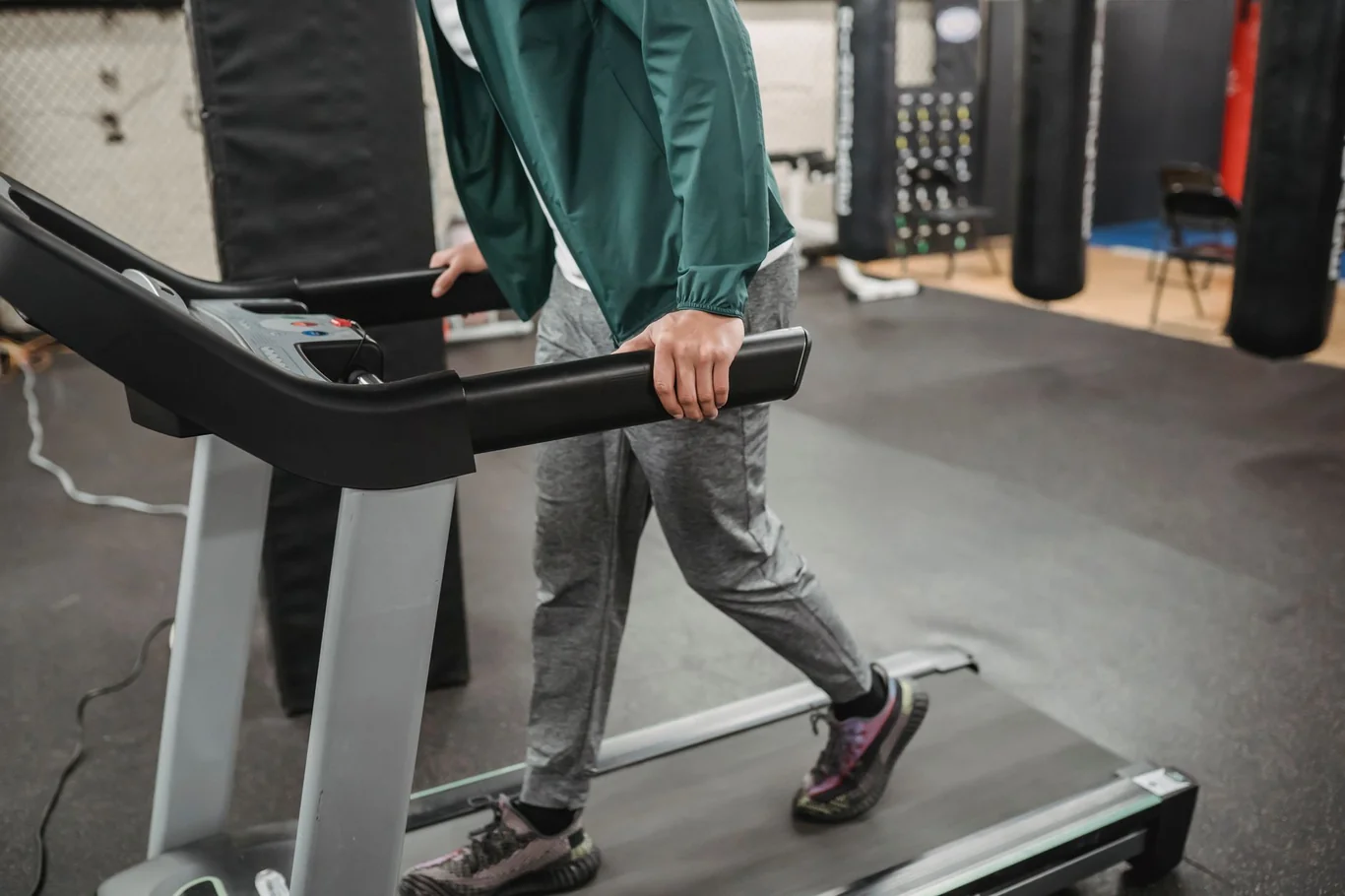 Person walking on a treadmill in a green jacket with hand on the console