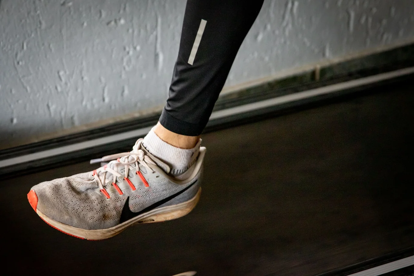 Runner's foot in a gray sneaker striking a treadmill belt mid-stride