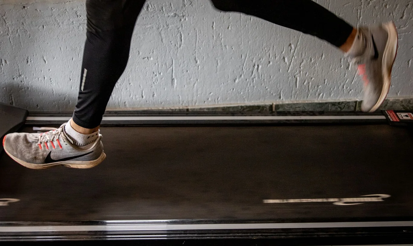 Runner's legs and feet in mid-stride above a treadmill belt in Nike sneakers