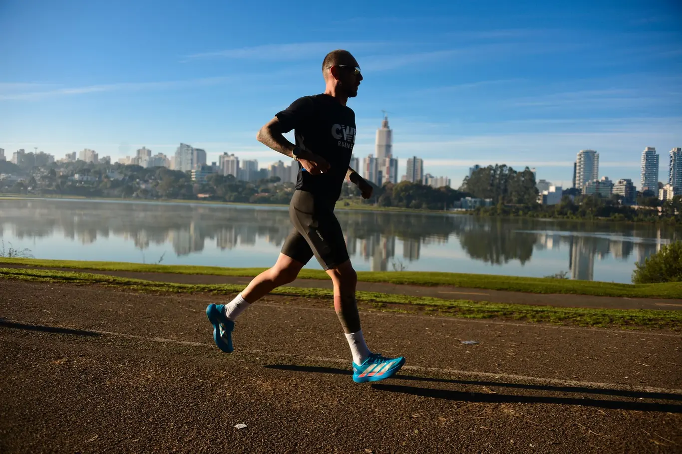 Man jogging along a waterfront path with a city skyline in the background