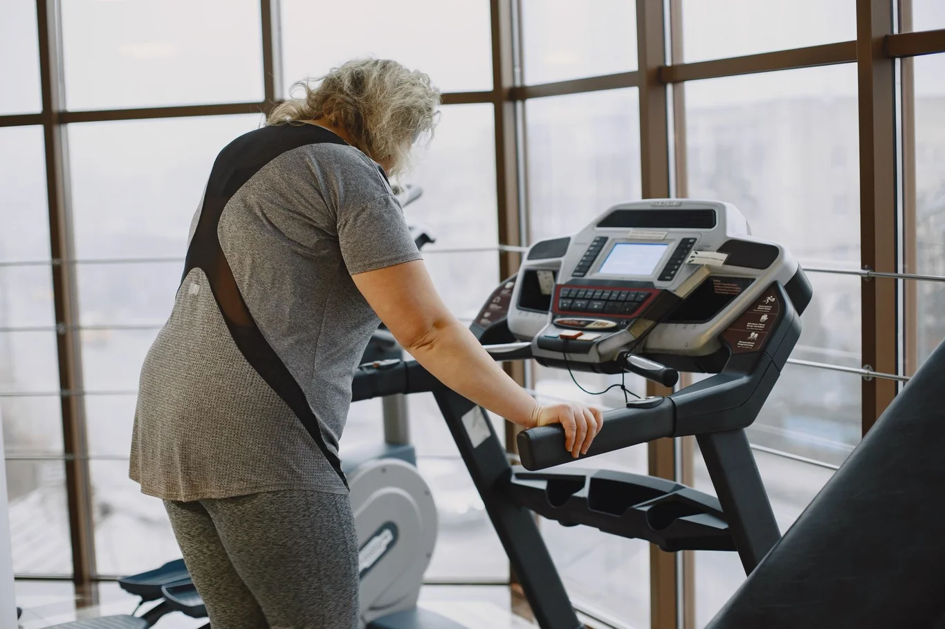Woman on a treadmill in a bright gym, resting her hand on the console