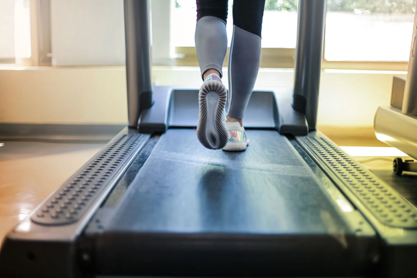 Close-up of running shoes and legs on a treadmill belt from behind