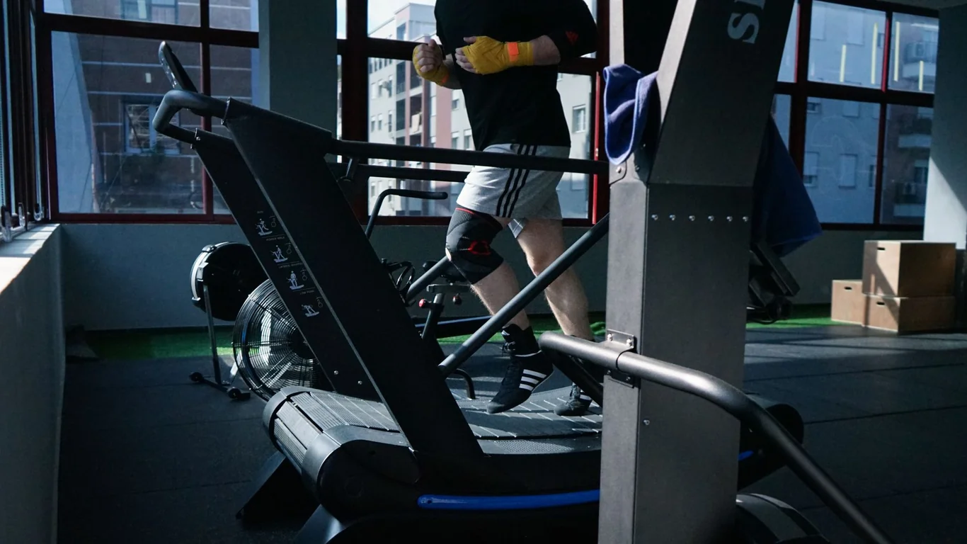 Man running on a gym treadmill wearing hand wraps near large windows
