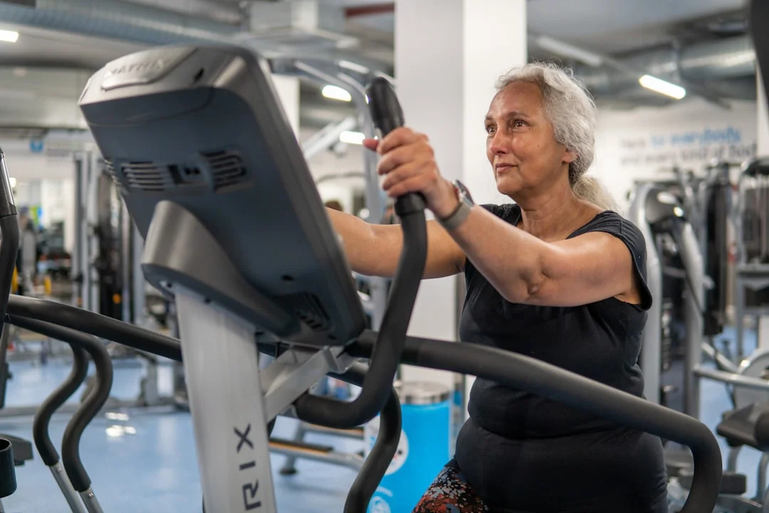 Woman using an elliptical trainer with a digital console in a busy gym