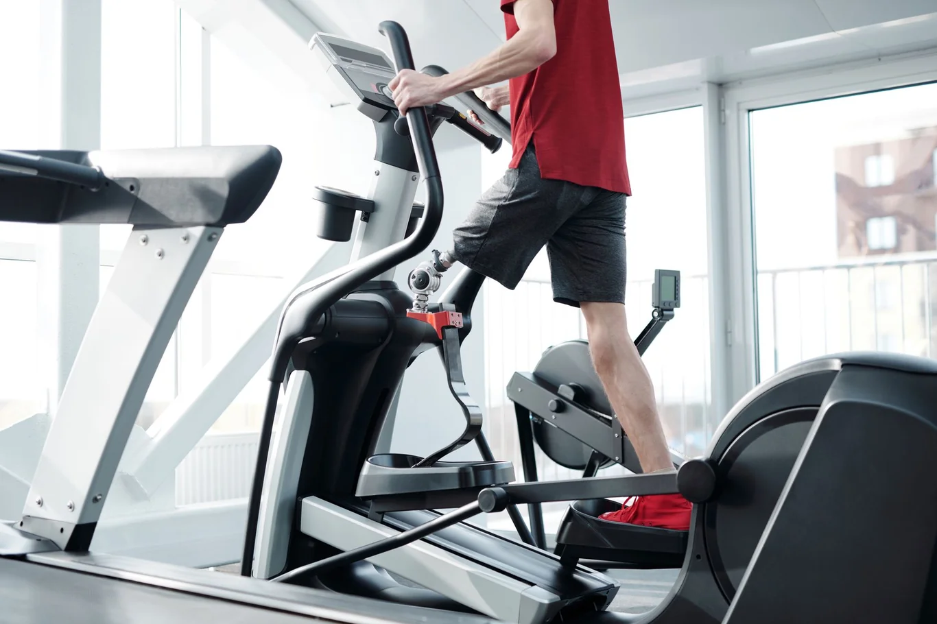 Man in a red shirt striding on an elliptical machine in a bright gym