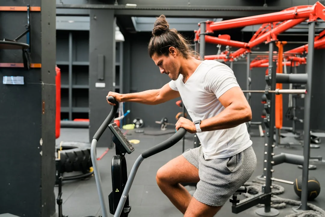 Man gripping elliptical machine handles while stepping in a gym with red equipment nearby