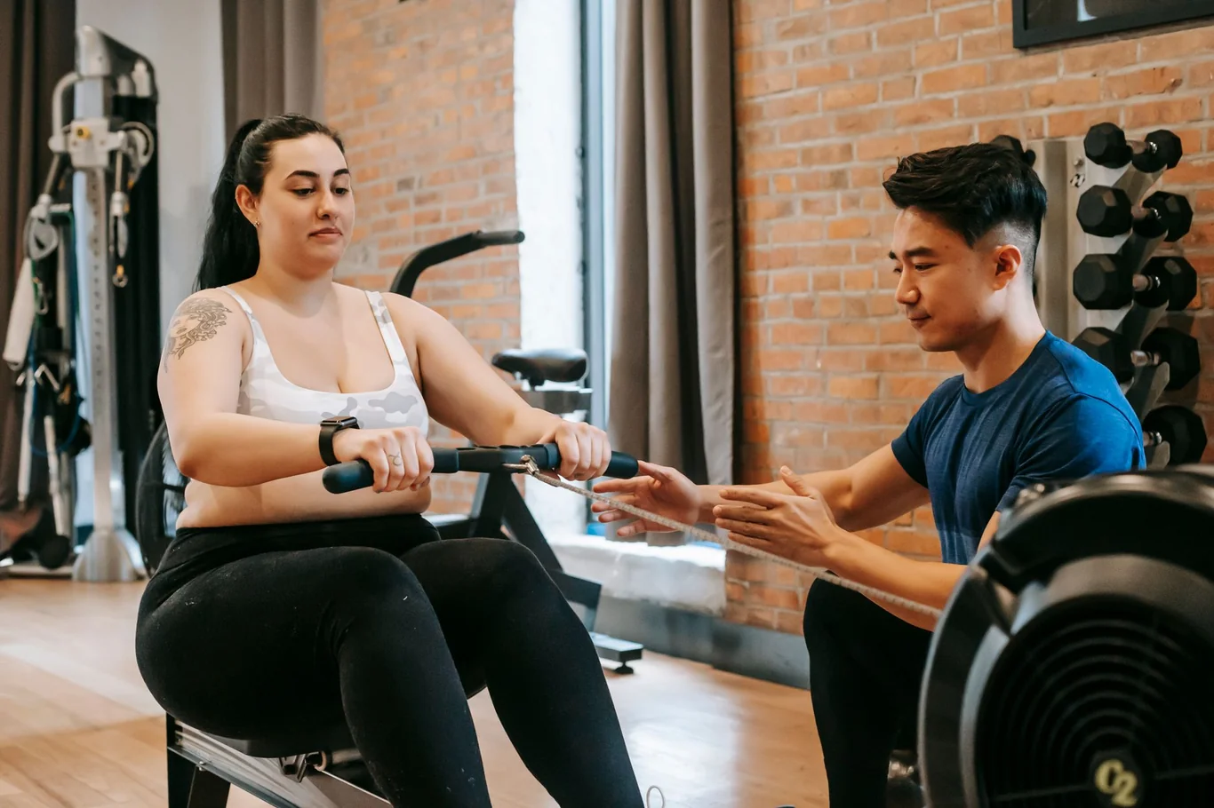 Woman using a rowing machine while a personal trainer coaches her rowing technique