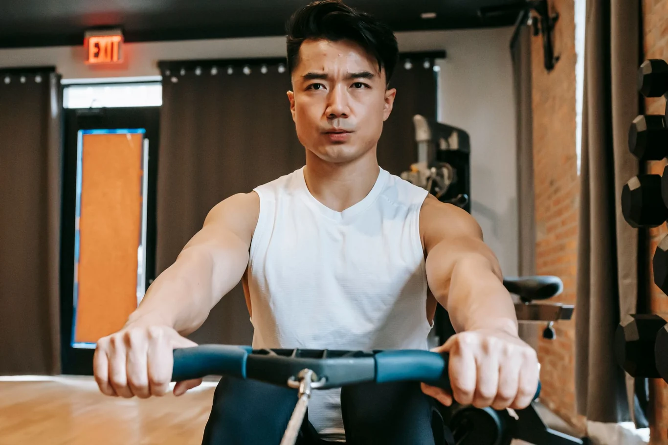 Man gripping the handlebar of an indoor rowing machine during a gym workout