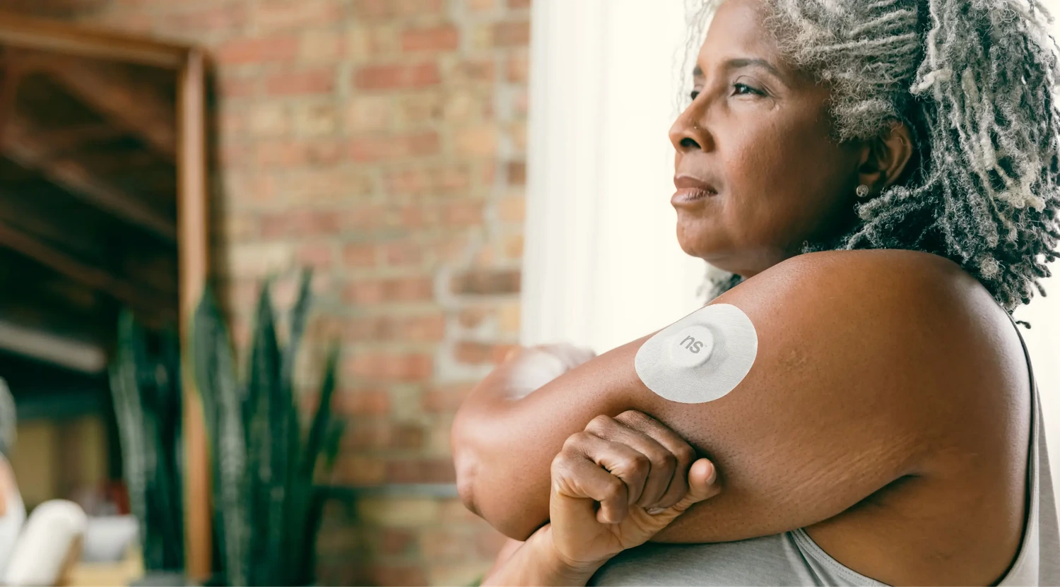 Continuous glucose monitor patch worn on a woman's upper arm indoors