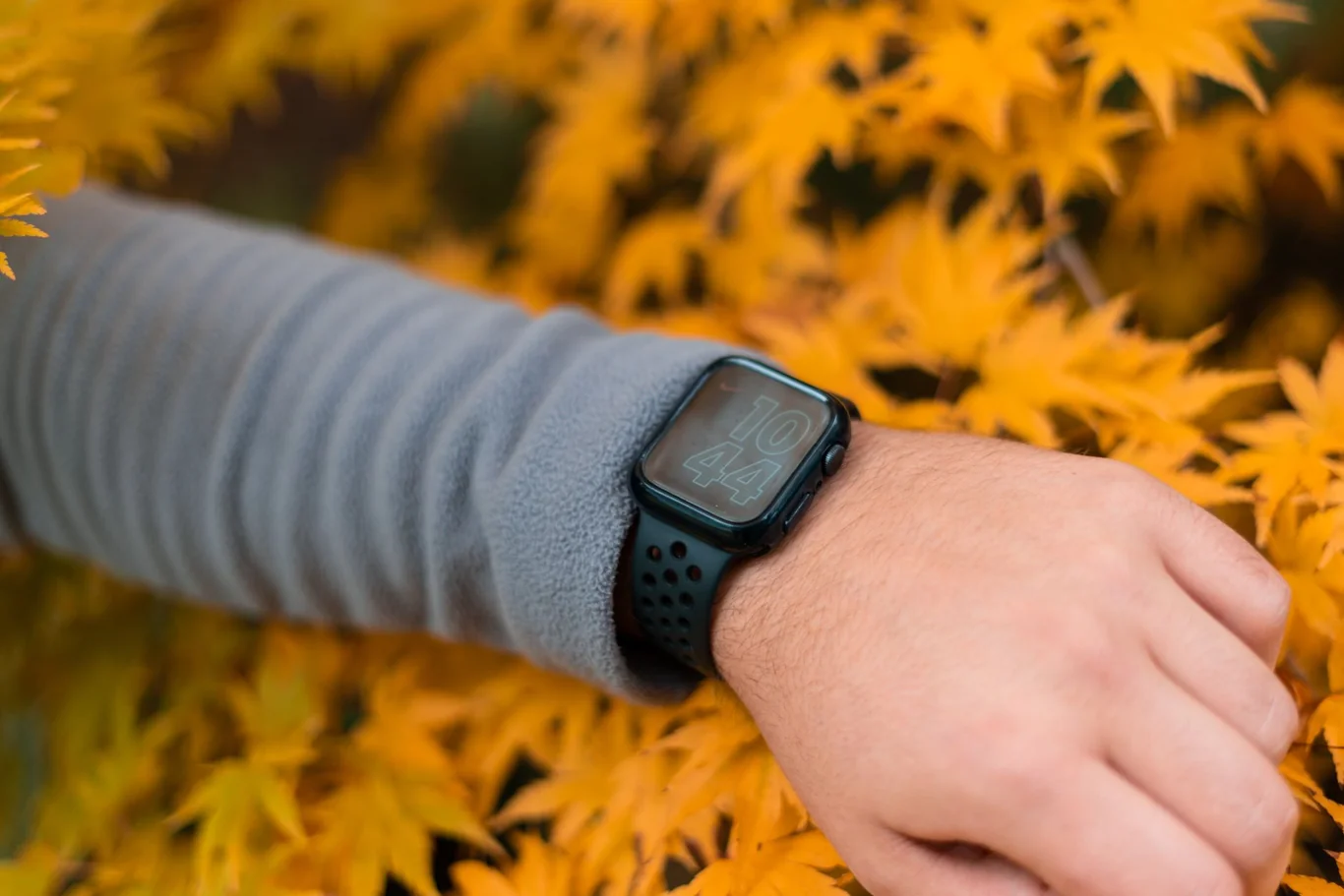 Person checking a black sport smartwatch display outdoors near autumn foliage