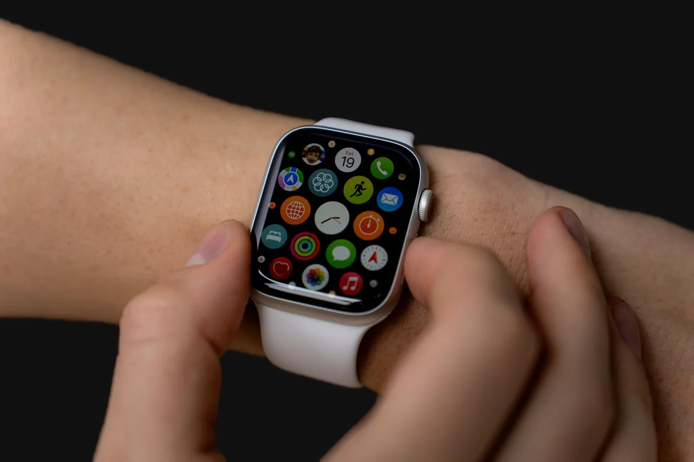 White smartwatch showing a grid of colorful app icons on a person's wrist