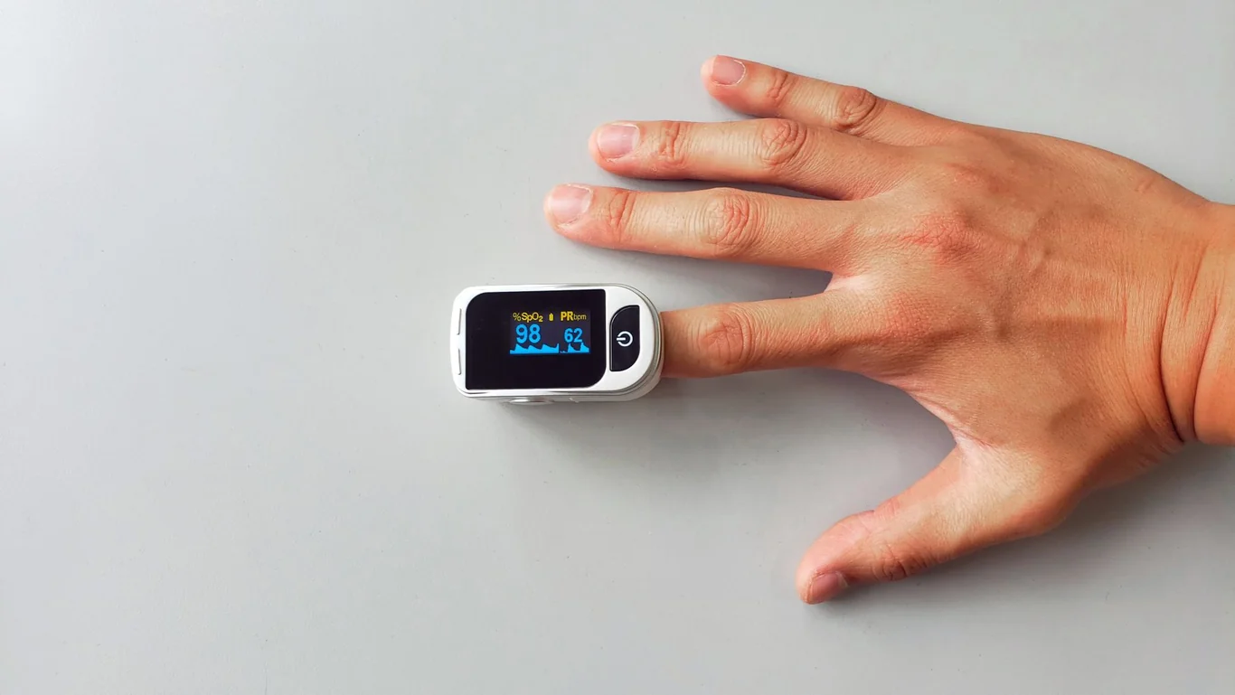 Hand with a fingertip pulse oximeter displaying blood oxygen and heart rate readings