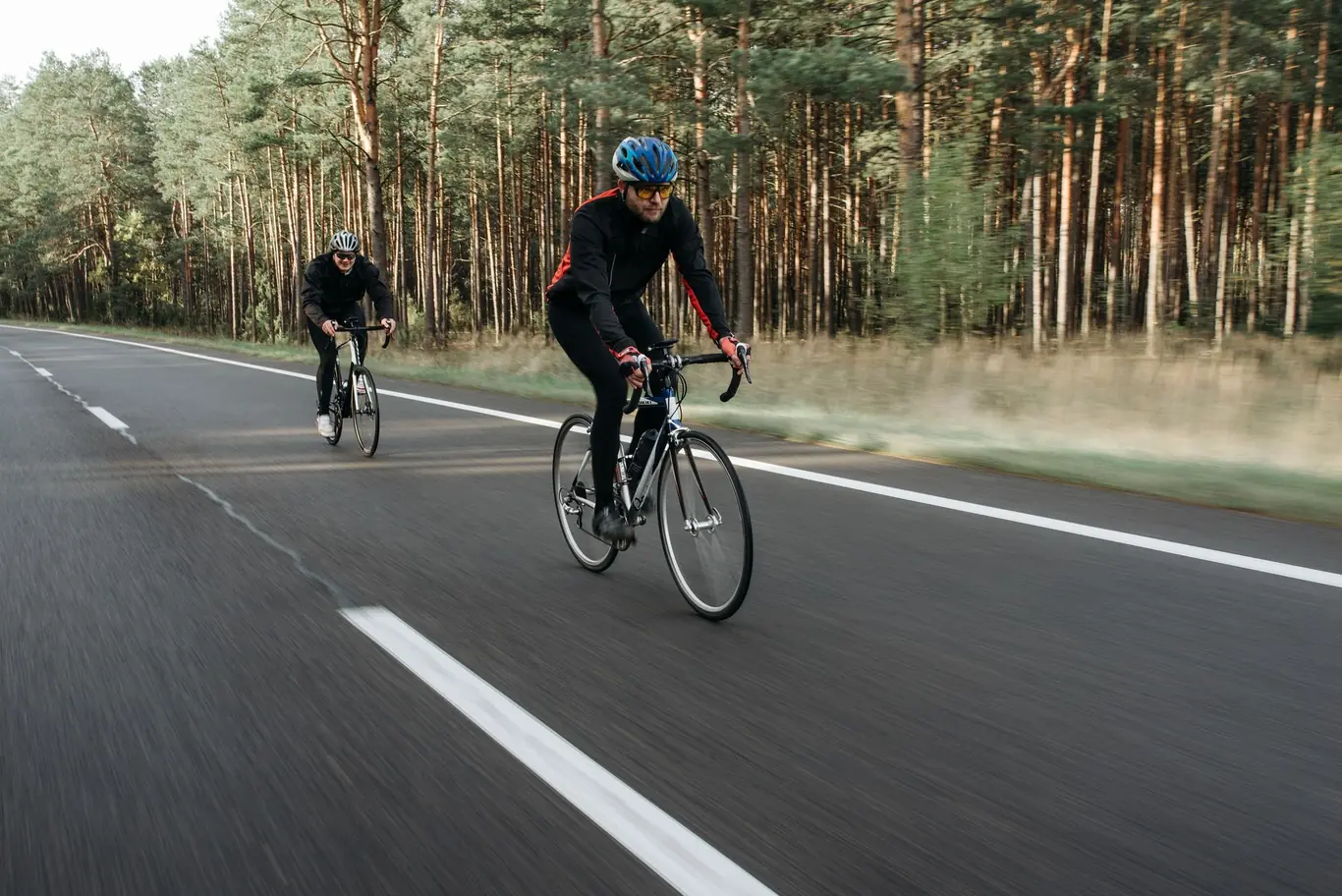 Cyclist riding a road bike along a forest road with motion blur in the background