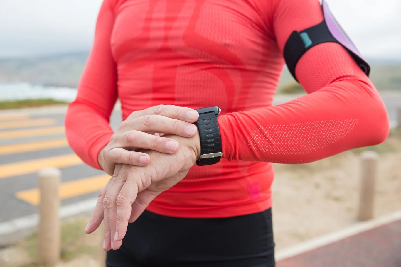 Runner in athletic gear checking a wrist fitness tracker outdoors
