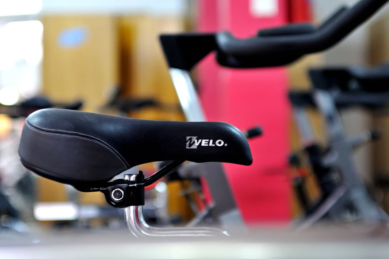 TVELO spin bike saddle and frame close up with other bikes in a gym