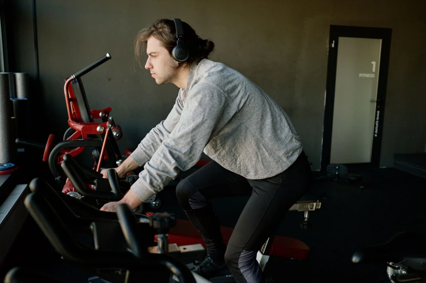 Person wearing headphones pedaling a red exercise bike indoors