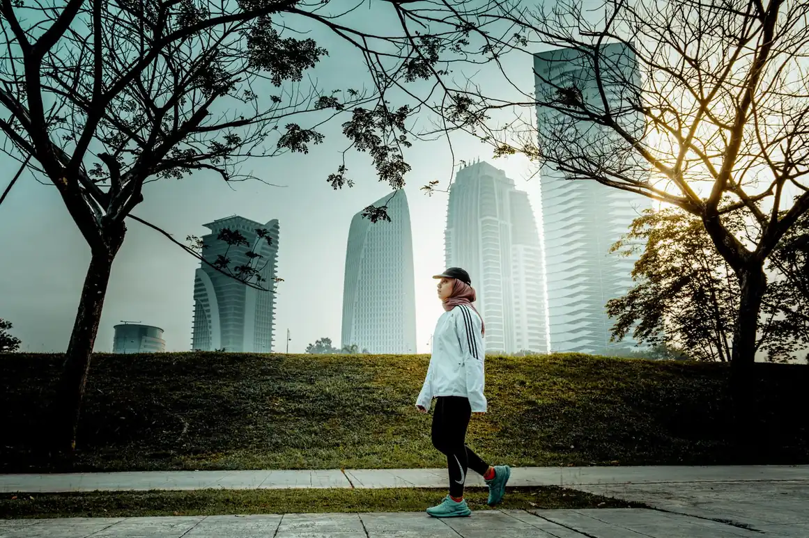 Woman in athletic wear walking outdoors with a city skyline behind her