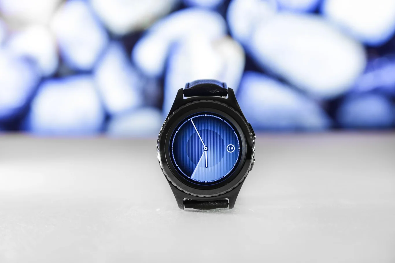 Black smartwatch with illuminated blue digital face on white surface