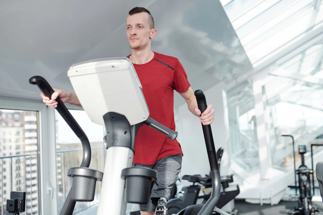 Man in a red shirt using an elliptical machine in a bright gym