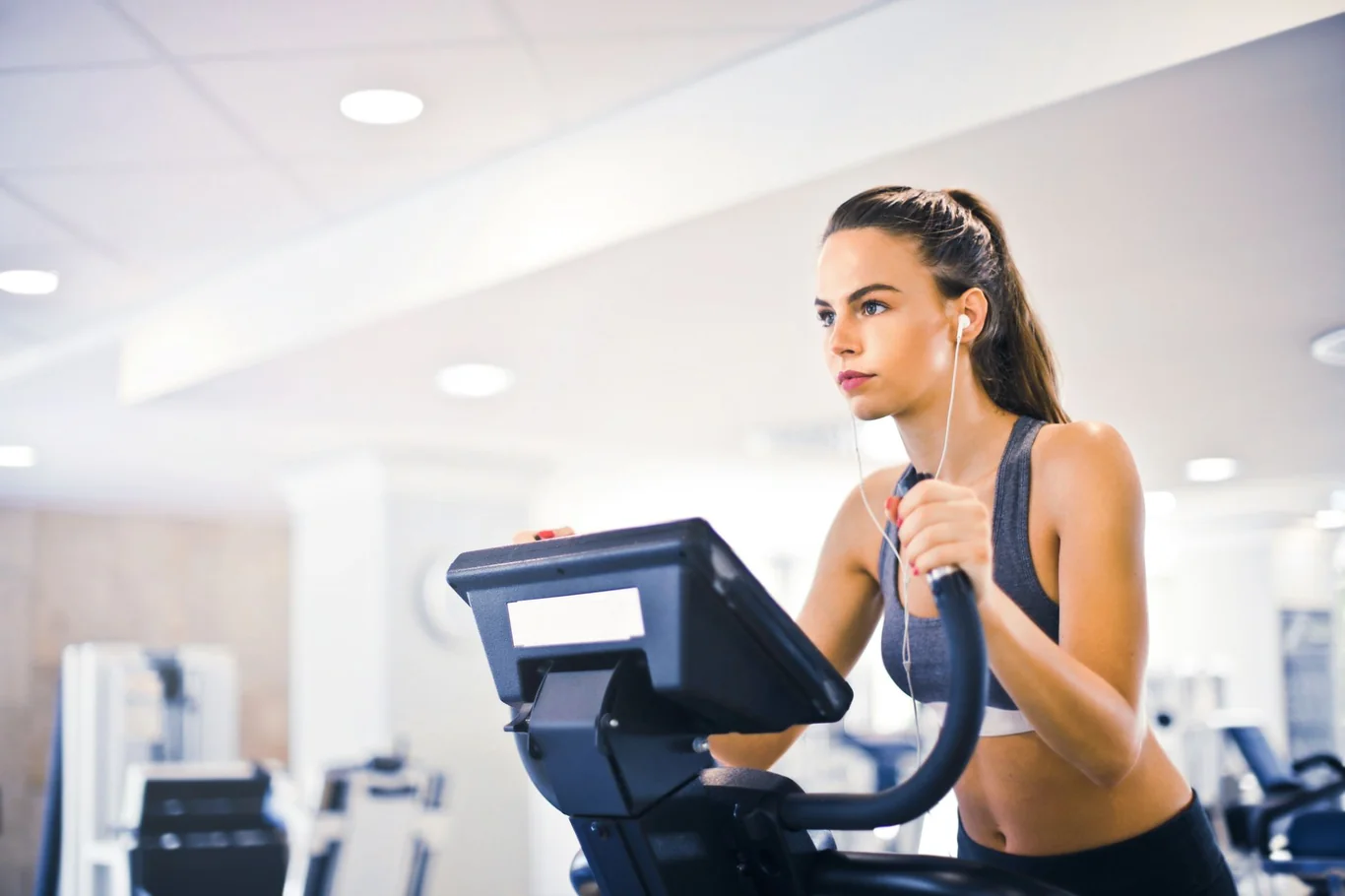 Woman using elliptical machine handles with wired earbuds in a gym