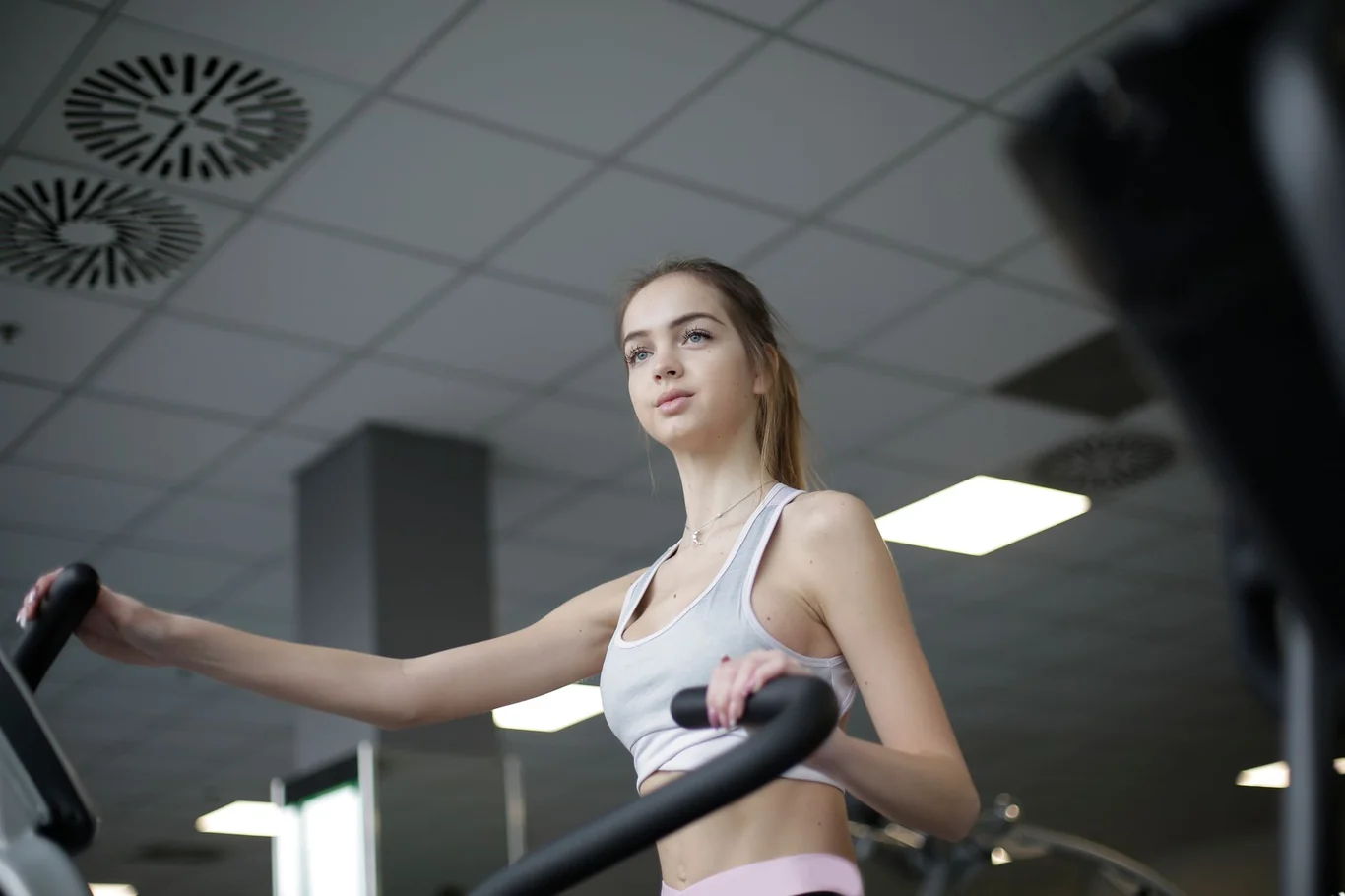 Woman gripping elliptical machine handles during an indoor gym workout