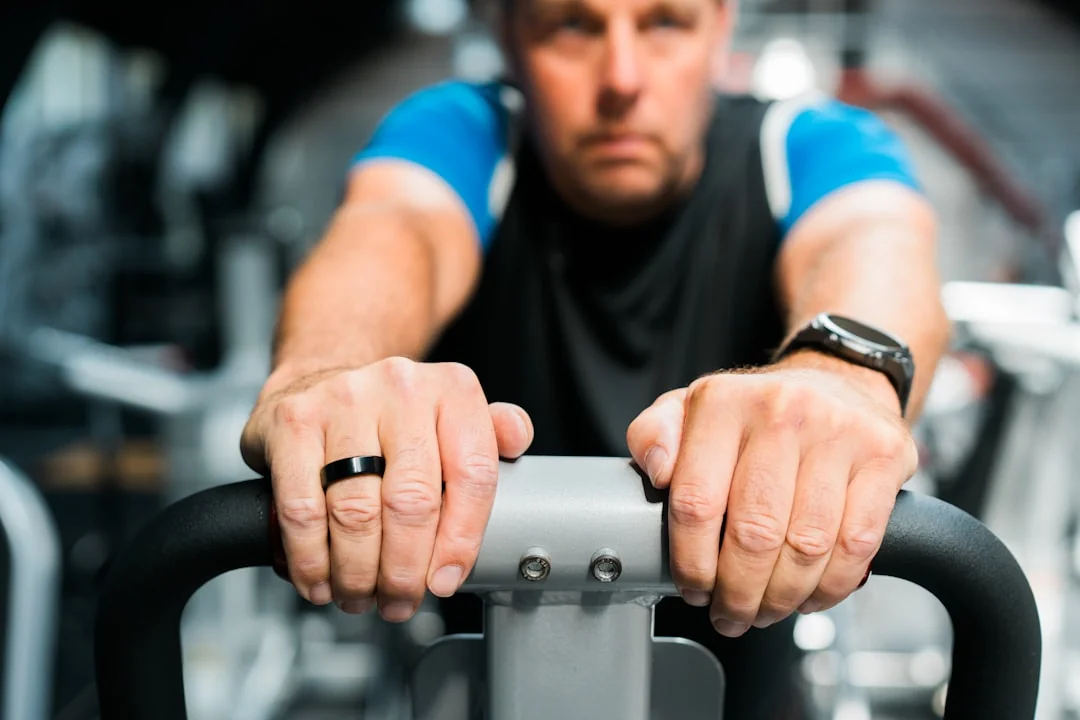 Man in a gym gripping the moving handles of an elliptical machine with a wristwatch visible