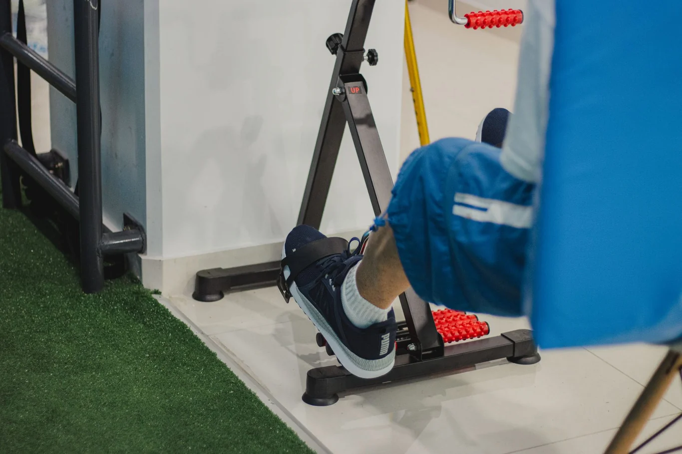 Foot resting on a black pedal exerciser with red rollers near a table leg