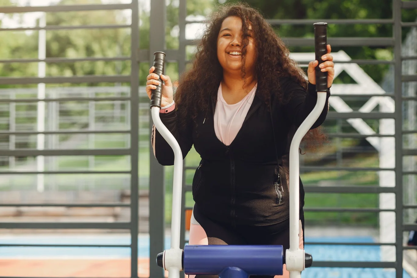Smiling woman gripping the handlebars of an outdoor elliptical trainer