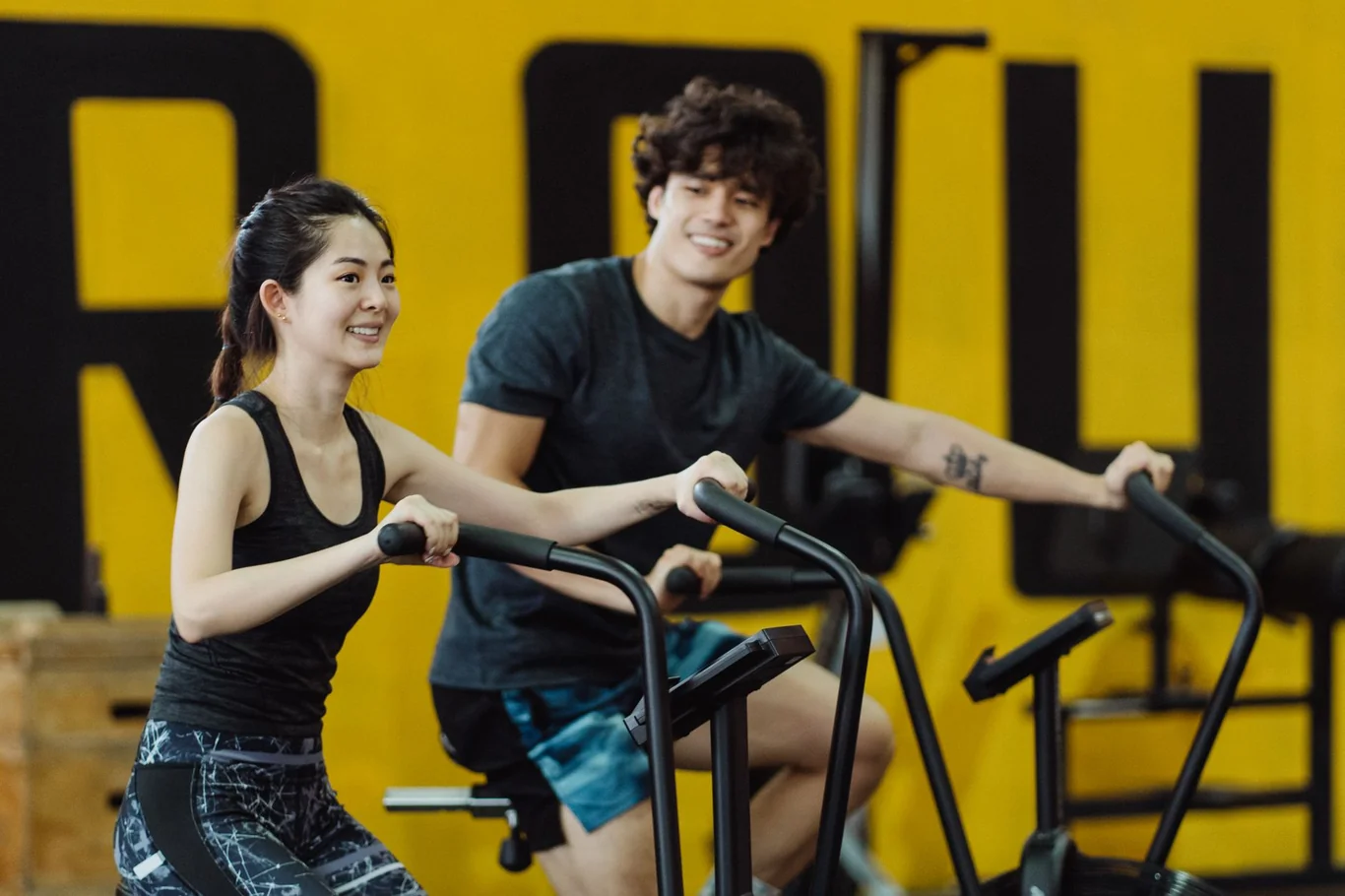 Man and woman working out side by side on elliptical cross trainers at the gym