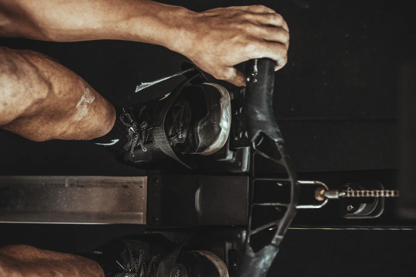 Feet strapped into rowing machine footplates while a hand grips the handle bar