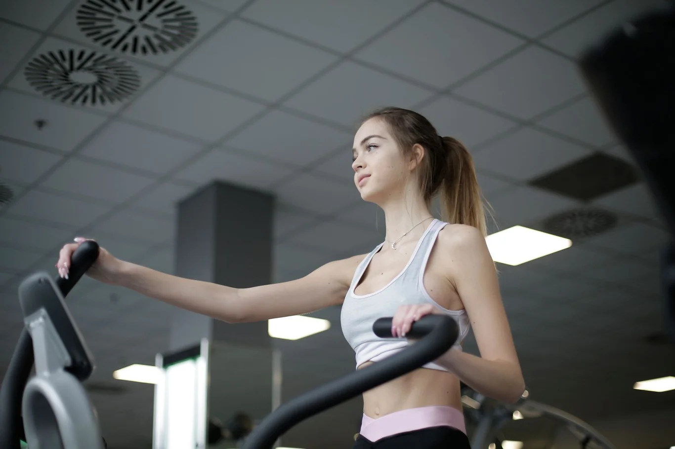 Woman gripping elliptical machine handlebars with her arm extended in a gym