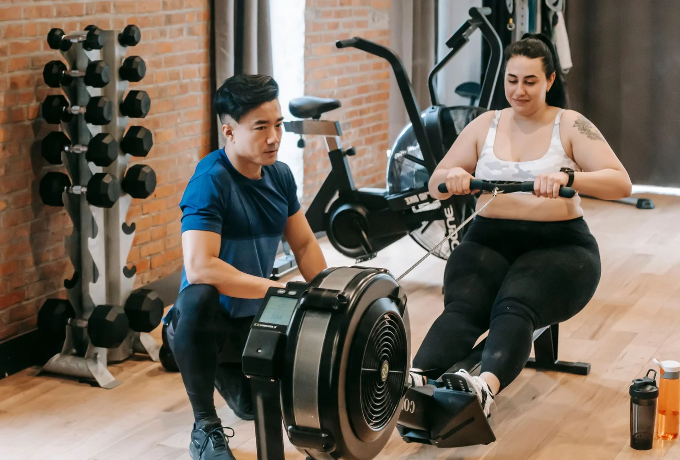 Personal trainer coaching a woman using a rowing machine in a brick-walled gym