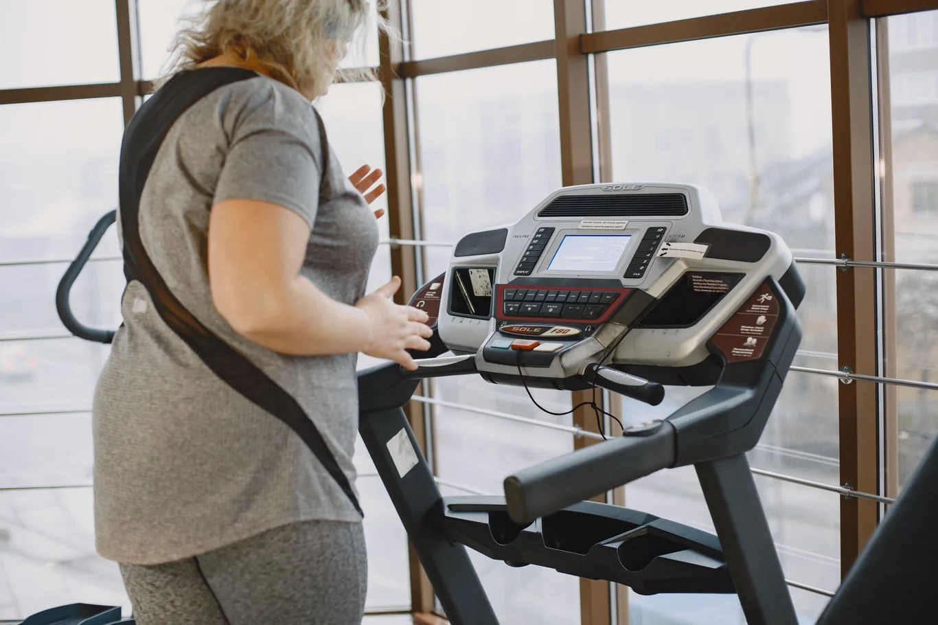 Person exercising on a treadmill in a home gym near large windows