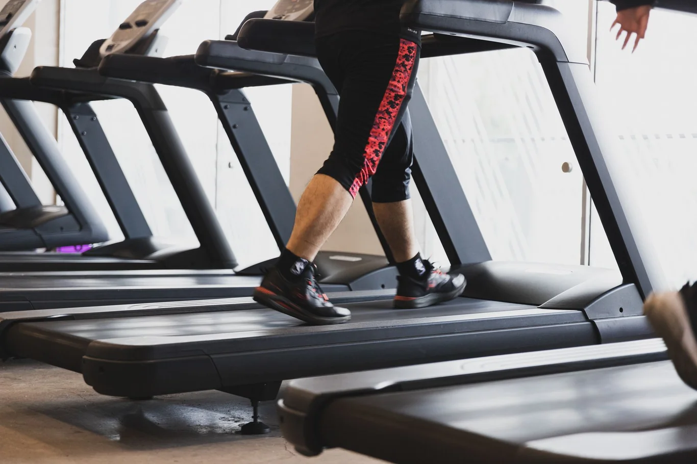 Runner's legs mid-stride on a treadmill in a row of gym cardio machines