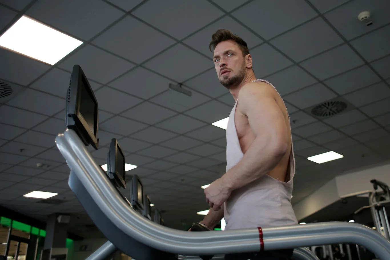 Man working out on a treadmill in a gym, gripping the side rails while watching the display