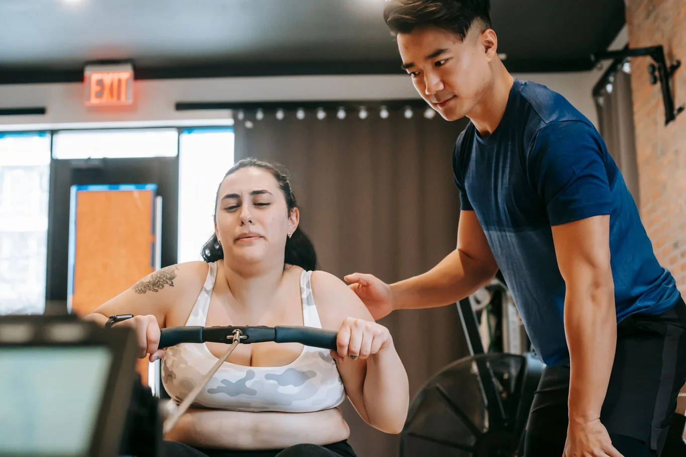 Woman using a rowing machine in a gym with a trainer coaching her form